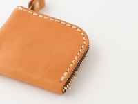 淺棕色皮革零錢包，帶有米白色縫線和金色拉鍊，包角處有皮革掛環。