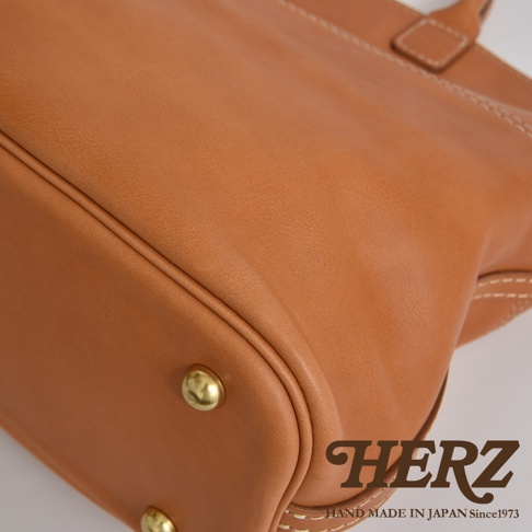 棕色皮革製作的職人手作兩用托特包，包身有著白色車縫線細節，底部裝飾有金屬鉚釘。