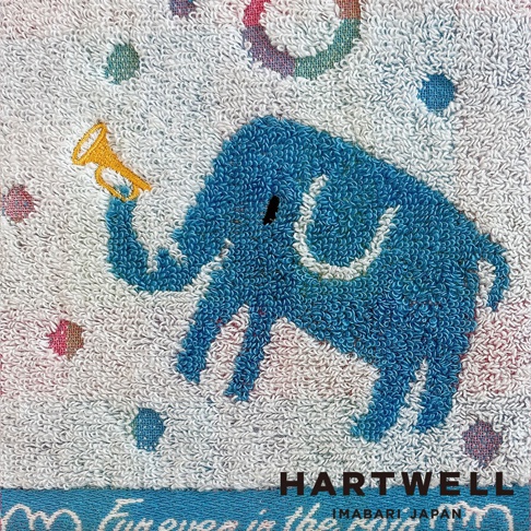這是一條白色的 Hartwell 今治毛巾，中央繡有一隻輪廓簡約的藍色小象，牠正用象鼻舉著一把黃色小喇叭，背景點綴著彩色圓點圖案，毛巾下方印有 Hartwell Imabari Japan 的品牌標誌。
