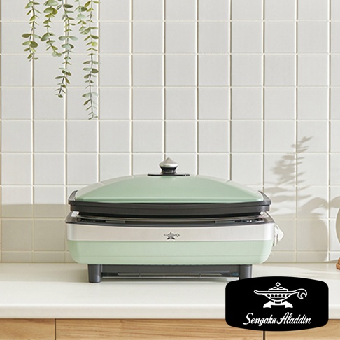 淺綠色及銀色機身的大烤盤，配有淺綠色鍋蓋及銀色把手，置於白色檯面上，背景為白色格紋牆面。