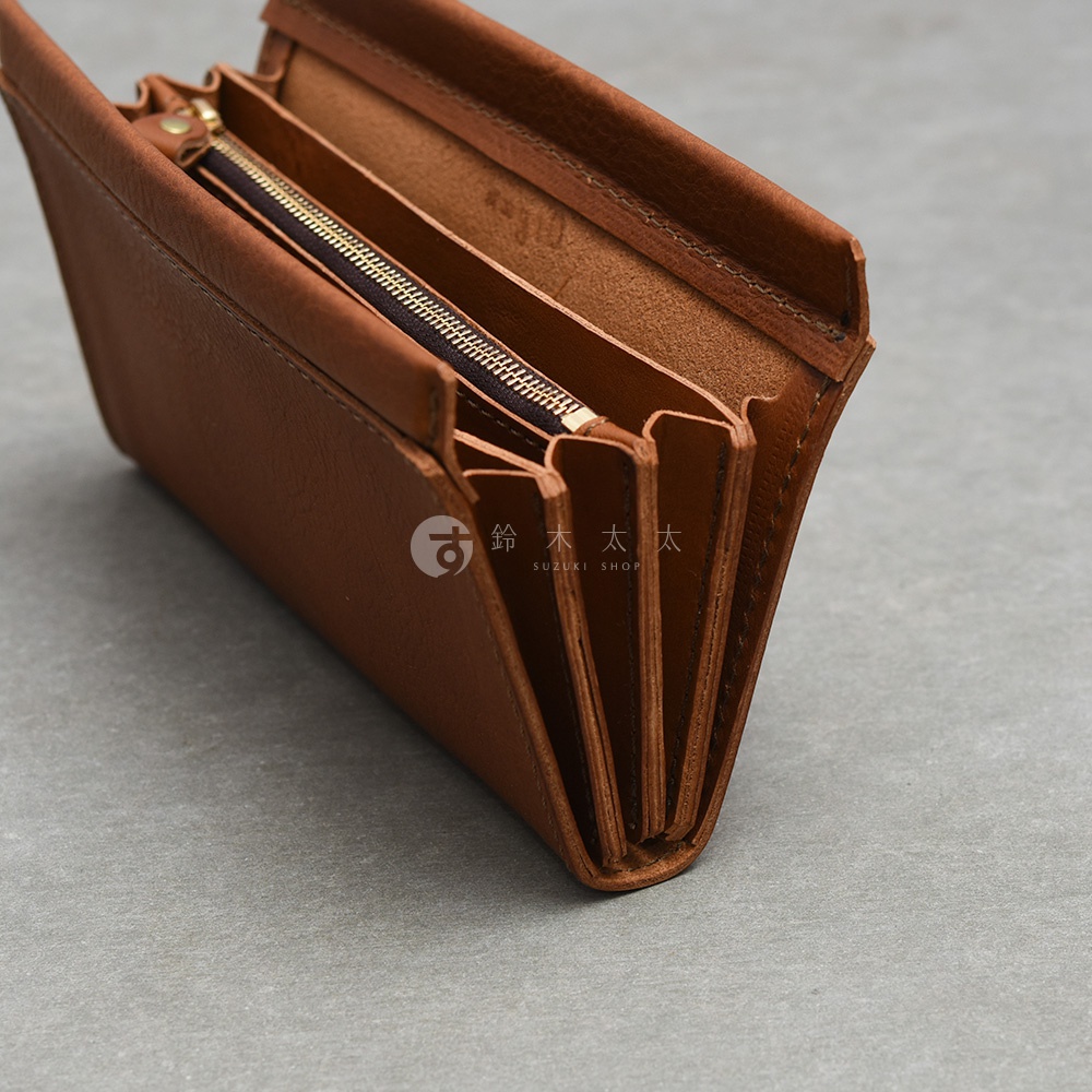 這是一個日本HERZ品牌的手作皮革長夾，呈現深棕色調，外觀為簡約的風琴式設計。從側面視角可以看到多層次的收納空間，內部搭配金屬拉鍊隔層，皮革質感細膩並帶有清晰的縫線細節，整體設計展現職人手工製作的穩重與耐用風格。