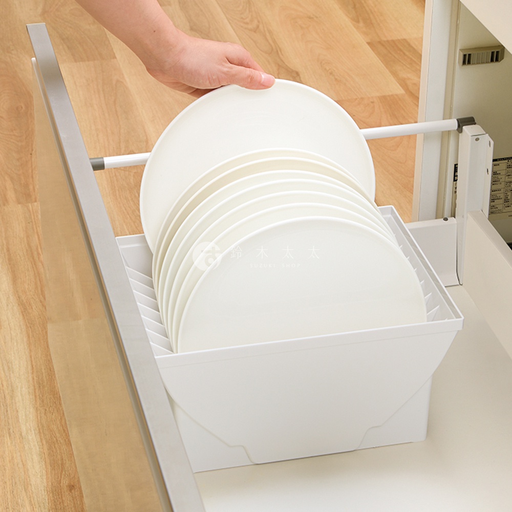 一個手正在將一疊白色盤子放入一個抽屜式收納架中，收納架位於一個淺色木紋的抽屜內。