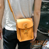 職人手作皮革休閒散步包，淺棕色，方形設計，翻蓋式開口，附有金屬扣環及皮質束帶，側邊與底部有縫線裝飾，肩背帶為皮質。