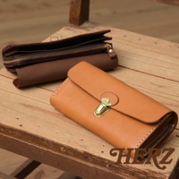 職人手作皮革長夾，採用溫暖的淺棕色皮革，搭配金色鎖扣。手風琴式設計，多卡層隔間，展現精緻工藝。另一側為深棕色皮革長夾，拉鍊開合。