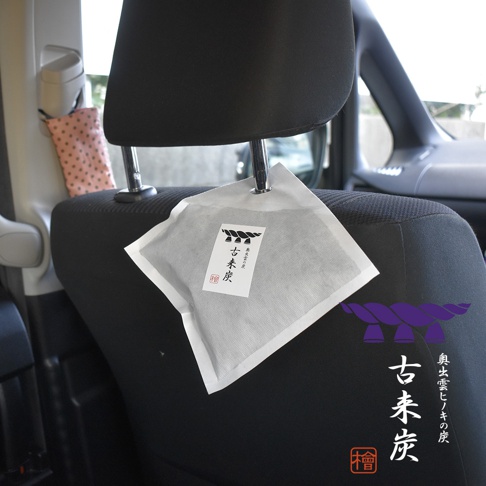 汽車座椅頭枕上懸掛著一個白色方形包裝的古來炭調濕木炭。包裝上有日文標籤，標示著產品名稱及圖騰。