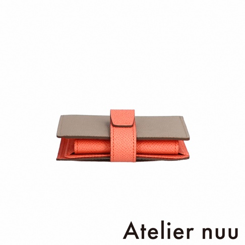 Atelier nuu 灰色與珊瑚橘色皮革雙折短夾，以珊瑚橘色皮革錶帶固定。