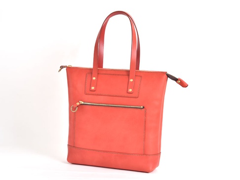 珊瑚紅色皮革威靈頓直式拉鍊托特包，設有雙提把、頂部拉鍊開合，前方有兩個拉鍊口袋，其中下方口袋配有金色圓形拉環。