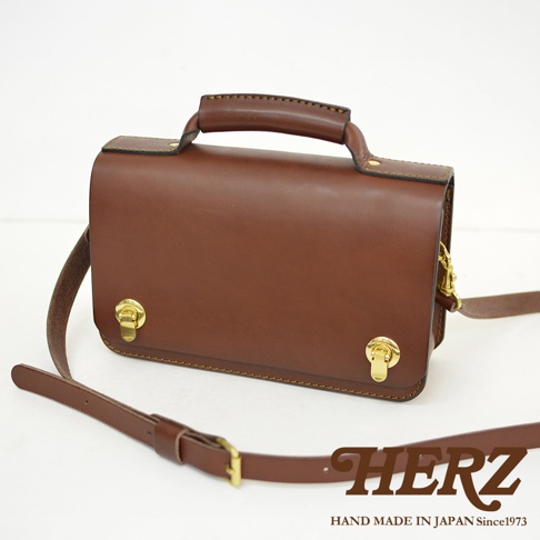 職人手作皮革經典兩用雙扣迷你單肩包，採用棕色皮革製成，配有頂部手柄和可調節的斜挎肩帶，以及兩個金色旋轉鎖扣。