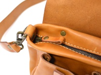 淺棕色皮革製成的肩背包，特寫拉鍊、銅色金屬扣環和皮革肩帶。
