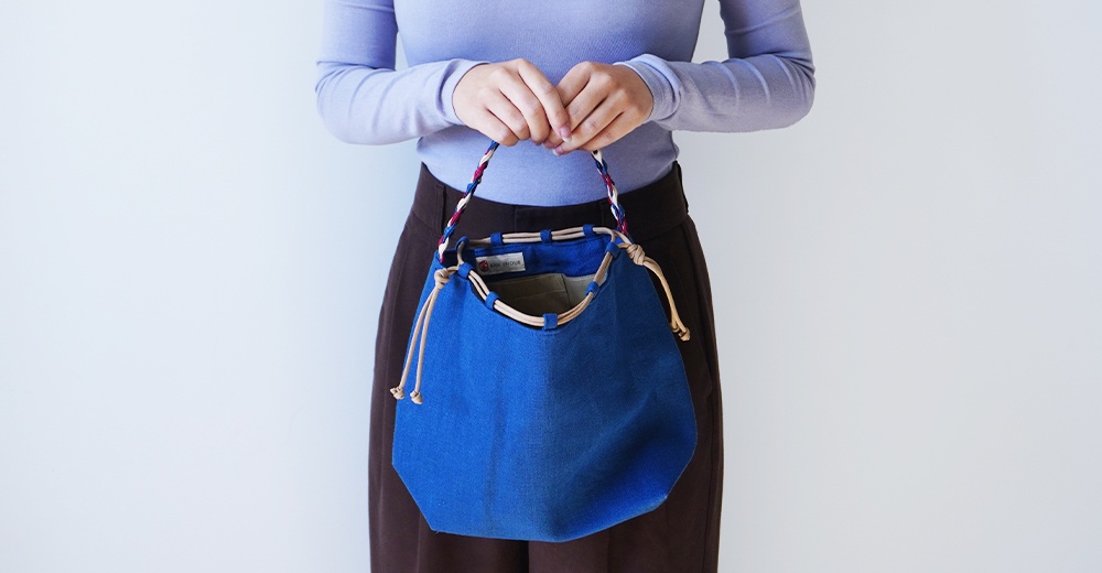 麻花辮束口手提包，由 BAN INOUE 品牌推出，以藍色帆布材質製成，並搭配繩飾與雙辮提把，展現獨特設計。