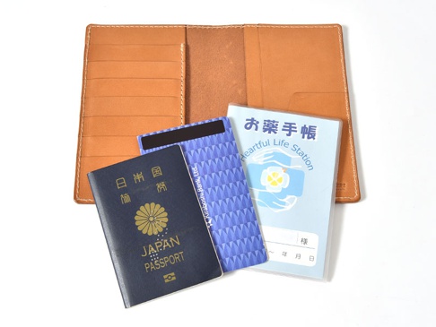 職人手作皮革多用途收納長夾 (KB-5) 內有深棕色皮革，可容納一本藍色日本護照、一張藍色幾何圖案的卡片，以及一本淺藍色標有日文及英文「Heartful Life Station」的藥品手冊。