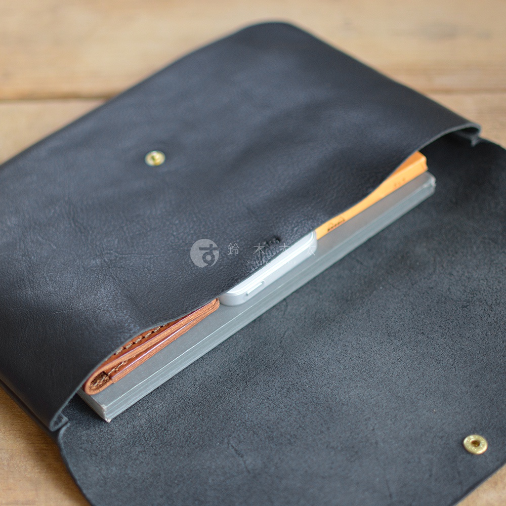 黑色皮革小物收納袋，有鈕扣設計，內部可放置筆記本及手機。