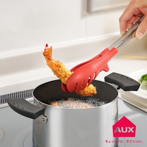 紅色的 UCHICOOK 不沾桌快手料理夾，夾著一塊炸好的蝦，上方有銀色的金屬手柄，下方是正在烹飪的鍋具。