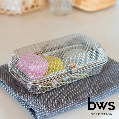 銀色不鏽鋼網製洗碗機專用清潔收納盒，內含粉色、黃色等顏色的清潔用品。收納盒帶有提把與夾扣，置於灰色織紋布上。