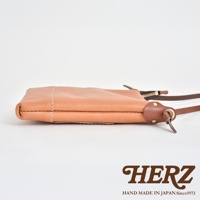 職人手作皮革直式隨身單肩包，淺棕色，側邊展示拉鍊與皮革背帶連接處，材質為真皮。