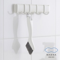 白色塑膠手柄的縫隙清潔刷，刷毛為灰色，刷頭傾斜，掛在白色掛架上，背景為白色磁磚牆面。