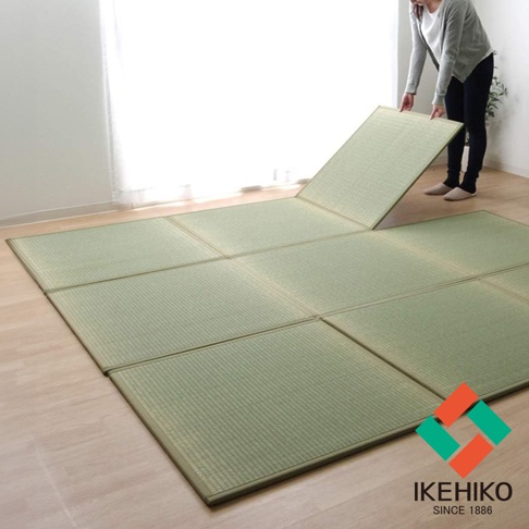 一片淺綠色、由藺草編織而成的組合式三折疊榻榻米地墊，鋪設在淺色木地板上，一角有品牌標誌。