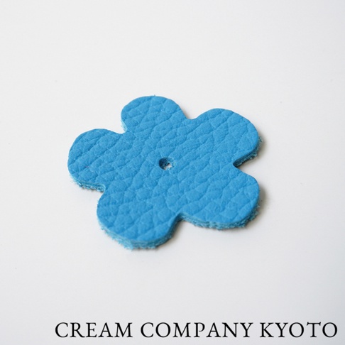 藍色皮革製作的花朵造型吊飾，表面有細緻紋理，中央有小圓孔，邊緣為未修飾的絨面，適合用於手提包等配件。