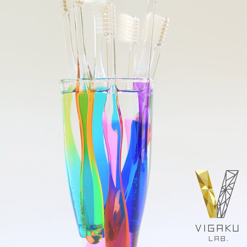 美學實驗室 VIGAKU LAB. 花系漸層植毛牙刷，透明杯中裝著彩色液體，多支不同顏色的牙刷並排置於杯中，牙刷和彩色液體在杯中交織出漸層效果，右側為美學實驗室的品牌 Logo。