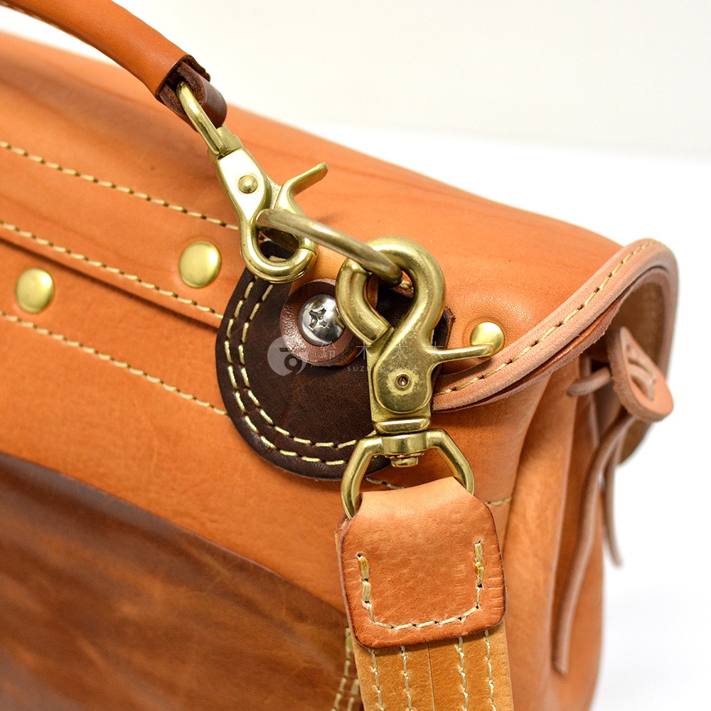 淺棕色皮革郵差包，特寫鹿角造型扣環、皮繩及撞色縫線，金屬配件為黃銅色。