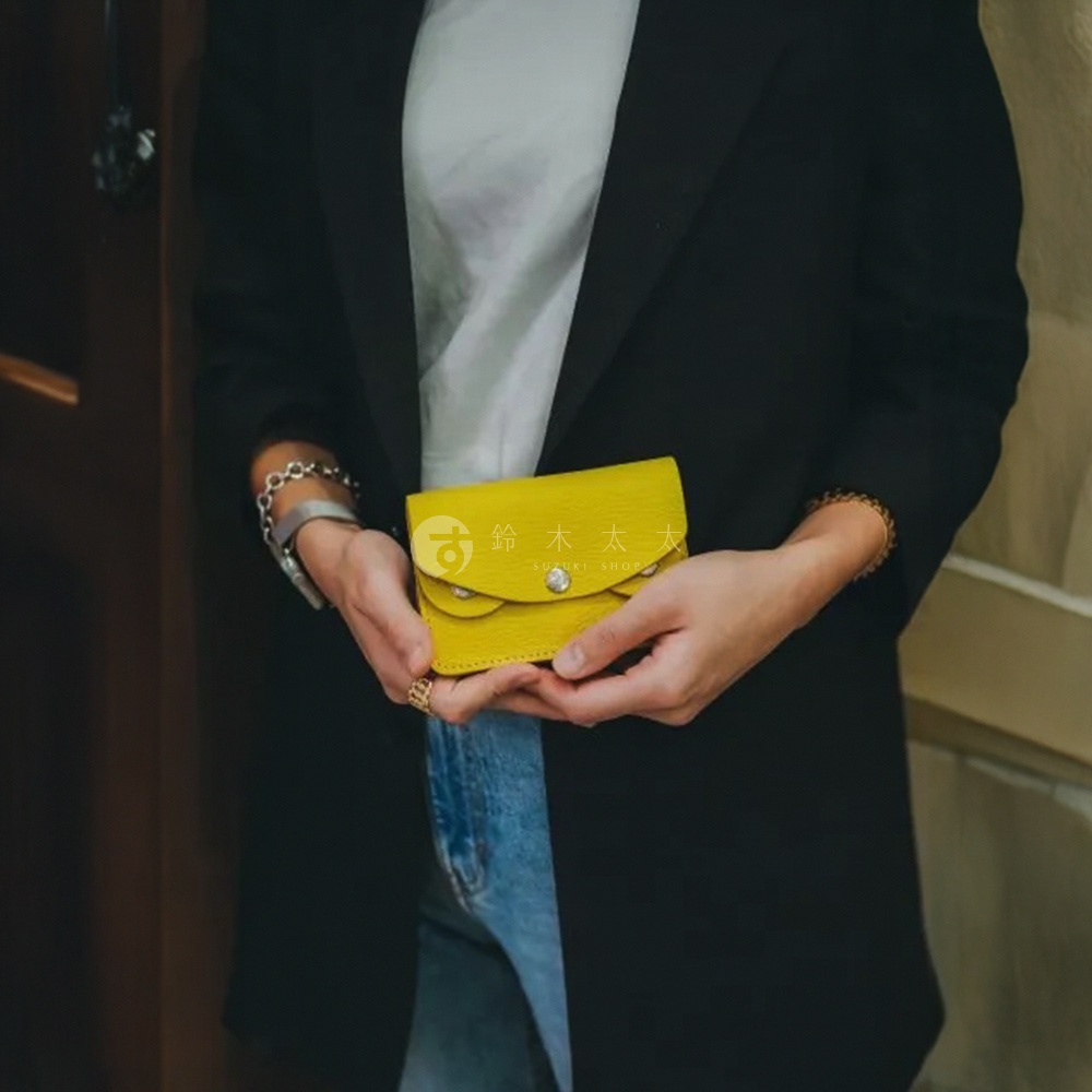 黃色皮革手作零錢包，有兩個金屬釦，包身帶有細緻紋理，由雙手捧著展示。