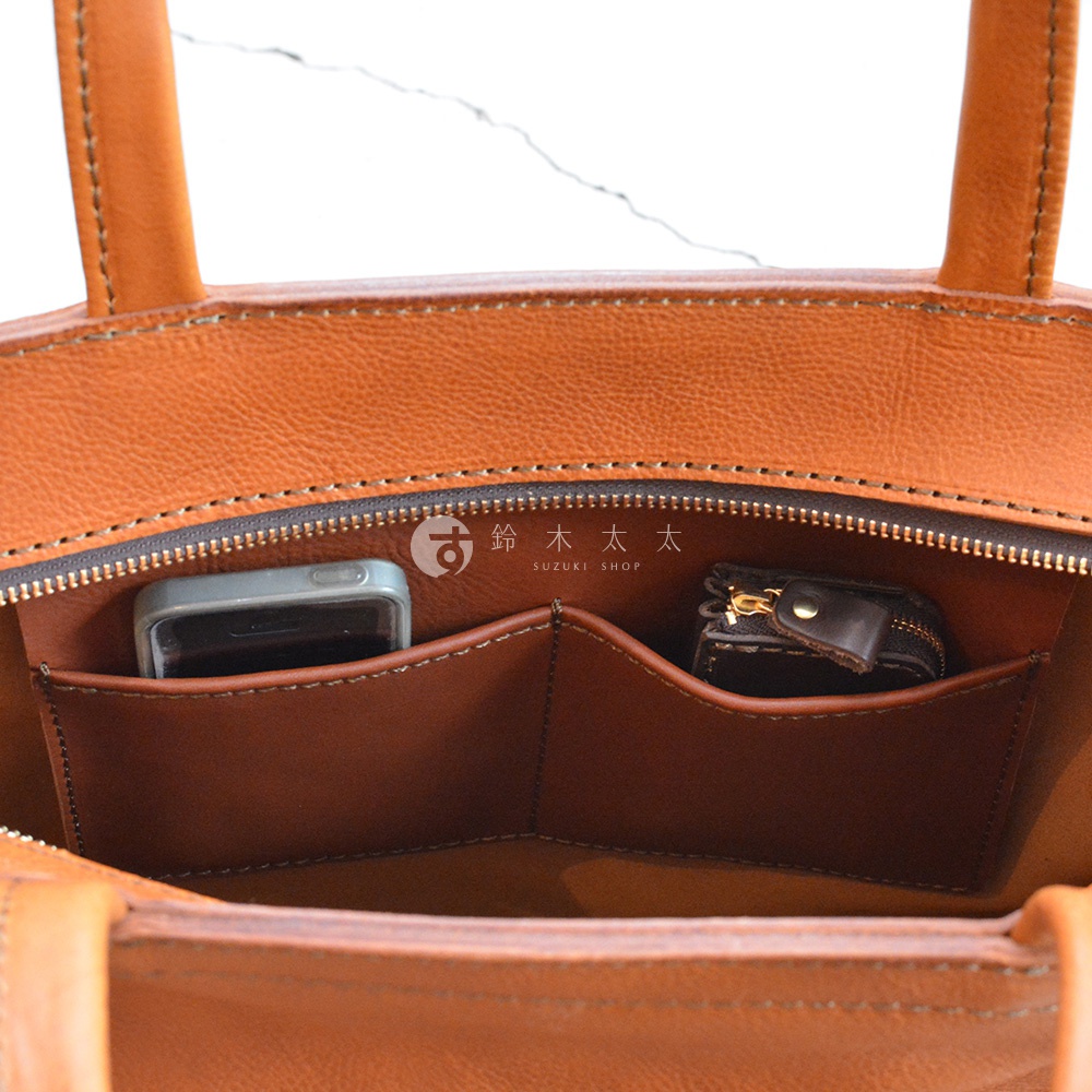 職人手作皮革Organ肩背拉鍊托特包內部，可見手機及零錢包放置於皮革隔層內，包包為橘棕色皮革材質。