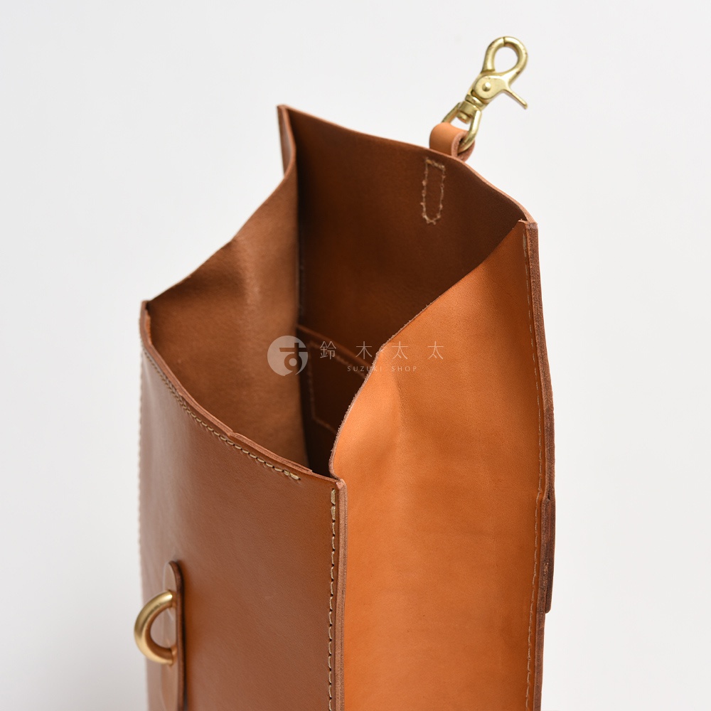 職人手作皮革紙袋風後背包 R-16，展示為焦糖棕色，材質為全真皮，包身線條簡潔，開口處配有黃銅色鉤扣與 D 型環。