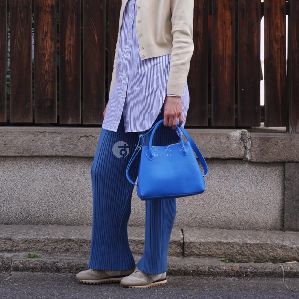 一位女性手持亮藍色皮革兩用手提托特包，包上有可拆卸的長背帶。