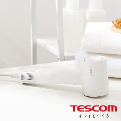 一個白色的TESCOM負離子吹風機，放置在白色桌面上，背景是白色毛巾和瓶子。
