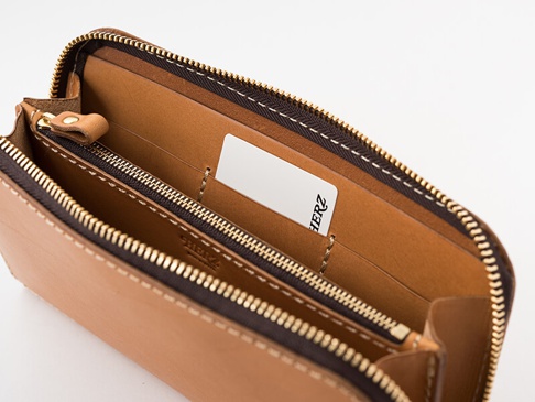 職人手作皮革大容量拉鍊長夾 (WL-5)，呈現自然棕色皮革，帶有精緻的車縫線和金色拉鍊，內部有多個隔層，其中一個隔層插有一張印有「HERZ」字樣的白色卡片。