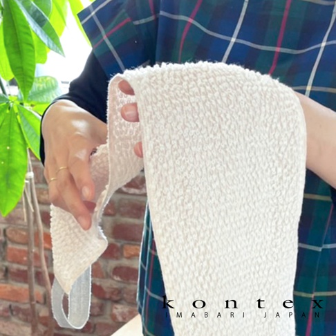 一條米白色、質地柔軟的天然素材按摩洗澡巾，表面有細小的紋路，一端有灰色織帶。