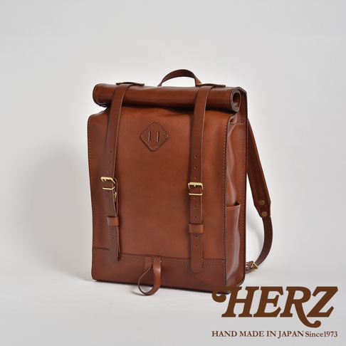 職人手作棕色皮革後背包，採用捲口設計，附有可調節式皮革肩帶、黃銅扣環，以及前方的菱形皮革飾片。