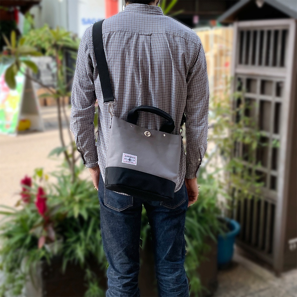 犬印純棉帆布兩用雙色托特包，灰色與黑色拼接，有手提和斜背兩種背法，包包上有一個白色標籤。