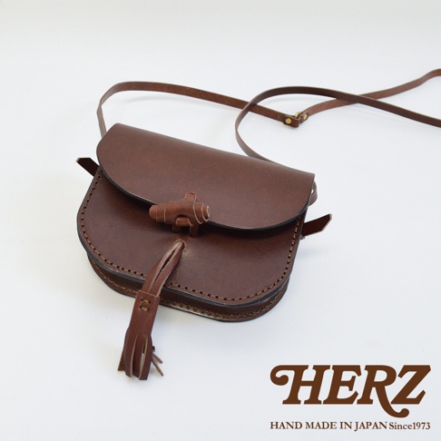 深棕色皮革流蘇側背包，採用馬鞍包造型，附有可調節的皮革斜背帶，包蓋處有獨特的木質鈕扣設計。