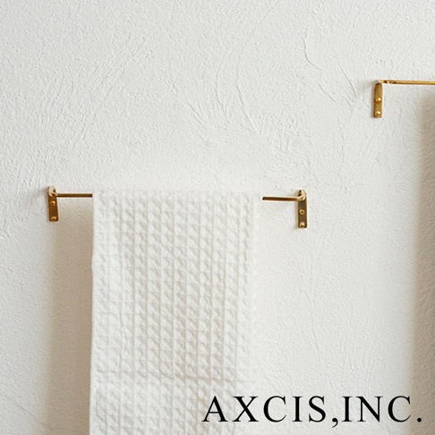 黃銅單桿毛巾架，設有兩組固定於白色紋理牆面上的小巧黃銅支架，其中一組掛著一條白色格紋毛巾。