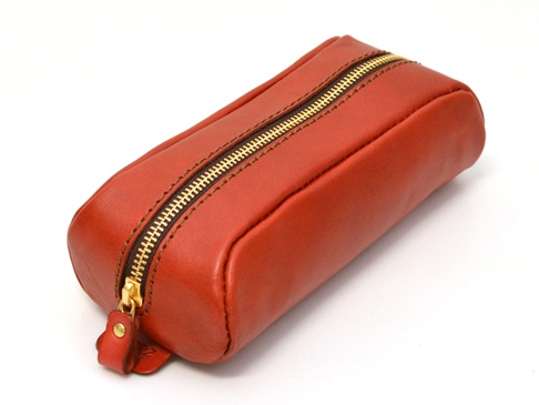 職人手作皮革圓角收納筆袋 (KP-1)，呈橘紅色，採用光滑皮革材質，搭配金色拉鍊及咖啡色縫線，造型簡約，尺寸約為長條形。
