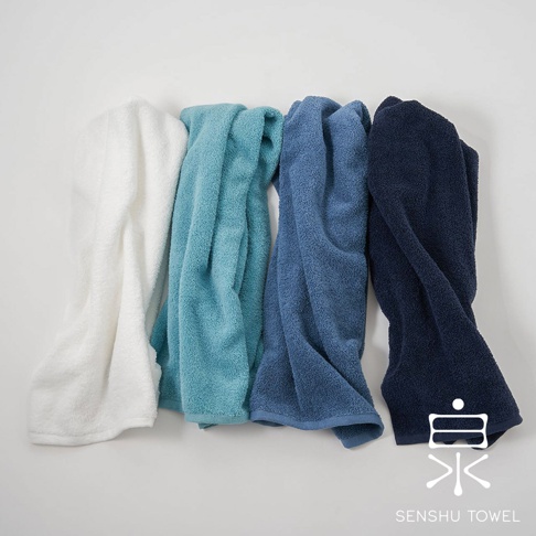 四條 envelopper 包裹溫柔高吸水長纖迷你浴巾，顏色分別為白色、淺藍色、藍色與深藍色，皆為毛巾材質，質地柔軟蓬鬆。