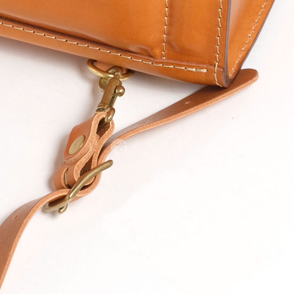 特寫鏡頭展示了棕色皮革包的細節，包括縫線、登山扣和皮革肩帶，以黃銅色五金件固定。