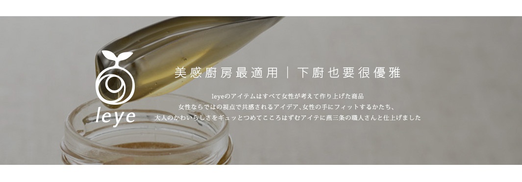 透明玻璃罐中裝有深色液體，上方有一個帶有白色品牌標誌的彎曲金屬夾，夾著一縷金黃色液體，背景為淺灰色。