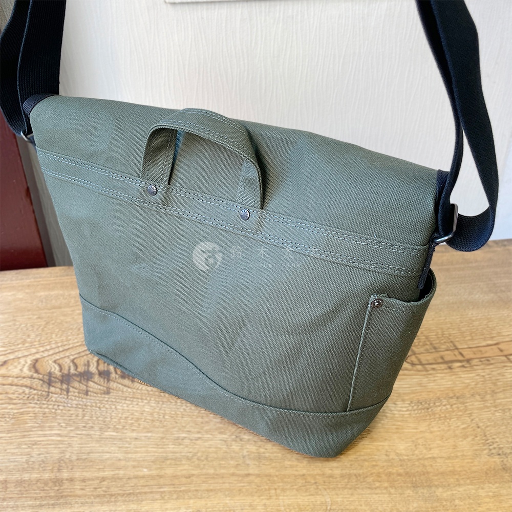 軍綠色純棉帆布製成的雙扣郵差包，設有提把與側邊口袋，搭配黑色肩帶。