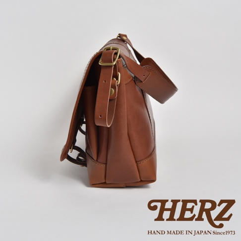 職人手作復古皮革郵差包，呈現天然皮革的溫潤棕色，帶有金屬釦環和可調節的皮革背帶，設計簡約實用。