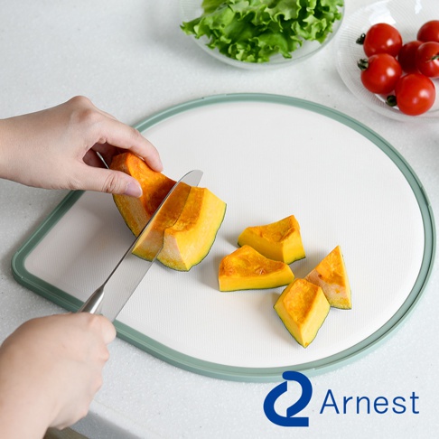 帶有淺綠色邊框的白色淚滴型砧板，上面放著幾塊切好的南瓜，一把刀正在切南瓜。