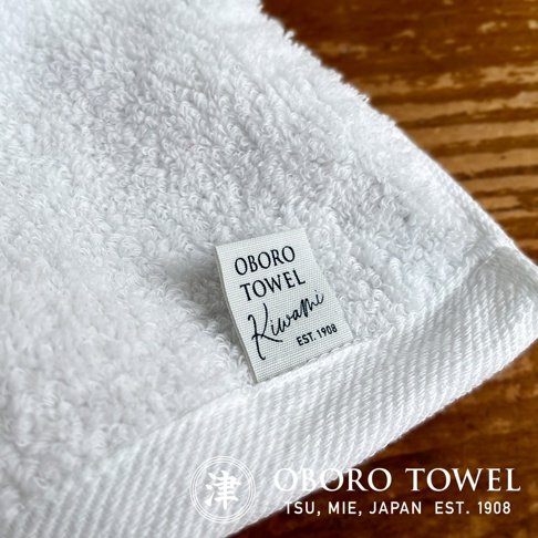純白色細纖毛巾，材質柔軟，毛圈蓬鬆。毛巾上縫有標籤，印有「OBORO TOWEL Kiwami EST. 1908」字樣。