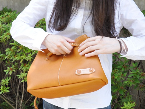 職人手作皮革可調式兩用托特包 (Q-14)，焦糖色皮革材質，束口設計，搭配白色縫線與皮革品牌標籤。