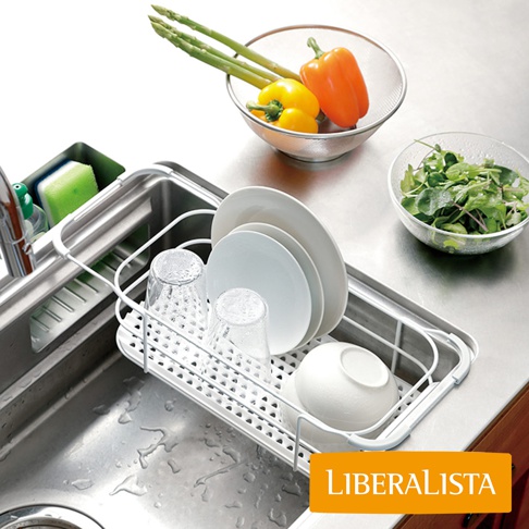 LIBERALISTA 水槽多功能瀝水籃架，上方擺放著清洗過的盤子、杯子和碗，籃架旁有綠色蔬菜、黃色和橘色甜椒，以及綠色蘆筍。