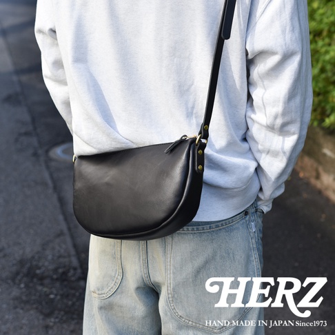 日本HERZ職人手作黑色皮革半圓馬鞍包，斜背於穿著淺灰色帽T和牛仔褲的模特兒身上