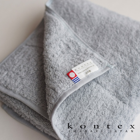 一張淺灰色極柔蓬鬆的今治大毛巾，帶有品牌標籤，標籤上印有「kontex imabari japan」字樣和日本國旗圖案。