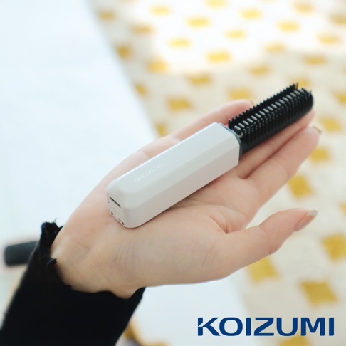 手持白色迷你瀏海梳，梳齒為黑色，梳子上有KOIZUMI品牌標誌