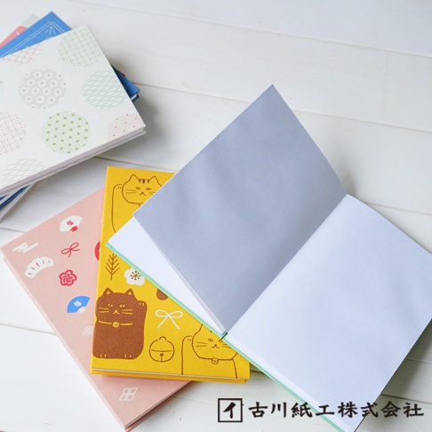 三本和紙製成的御朱印帳，封面分別印有日式傳統紋樣、招財貓圖案及日式吉祥圖飾，顏色包含白色、粉色、黃色和棕色，其中一本攤開，露出淺灰色和白色的內頁。
