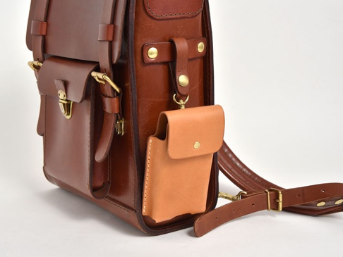 棕色皮革製成的手機收納包，附有可拆卸的淺棕色皮革小包，包身有金屬扣環和可調節的皮帶。
